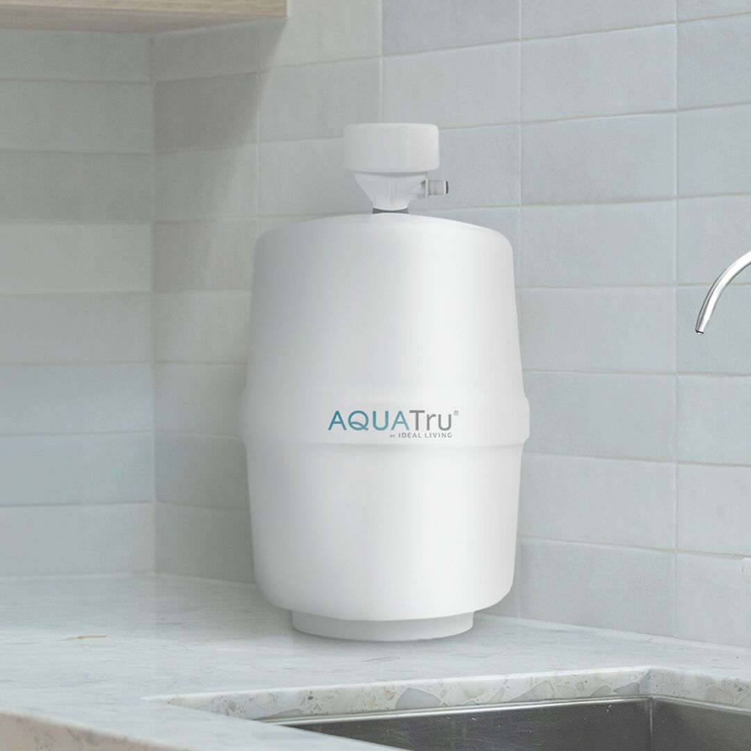 AQUATru undersink water filtration system on a countertop next to a faucet in a modern kitchen.