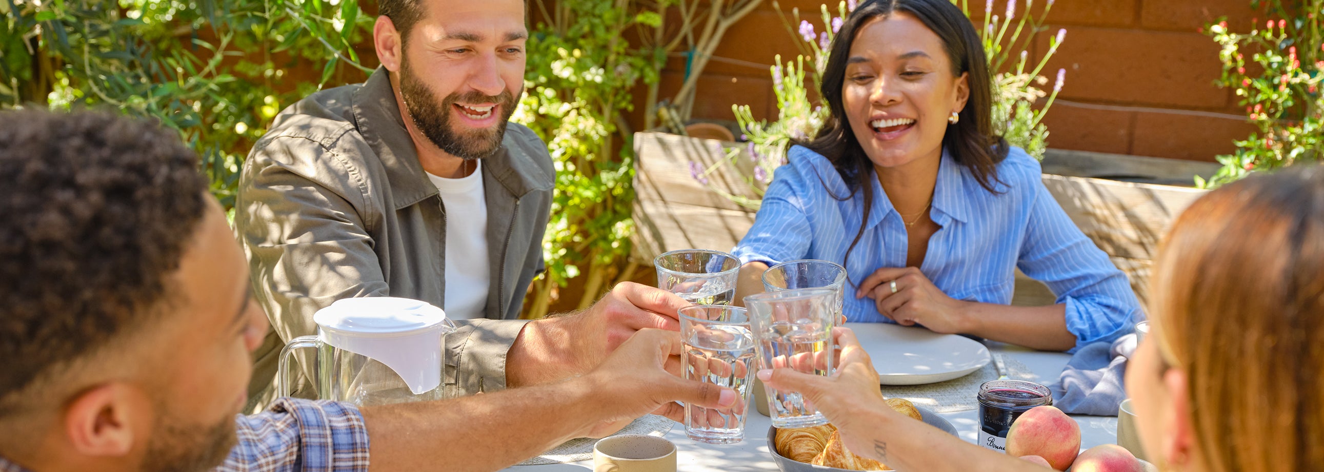 Friends toasting with glasses of water at an outdoor table, surrounded by greenery and food.
