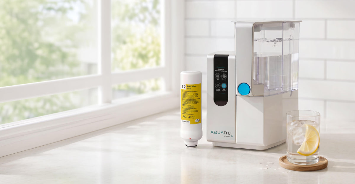 AQUATru water filtration system on a countertop with a glass of water and lemon slices beside it.