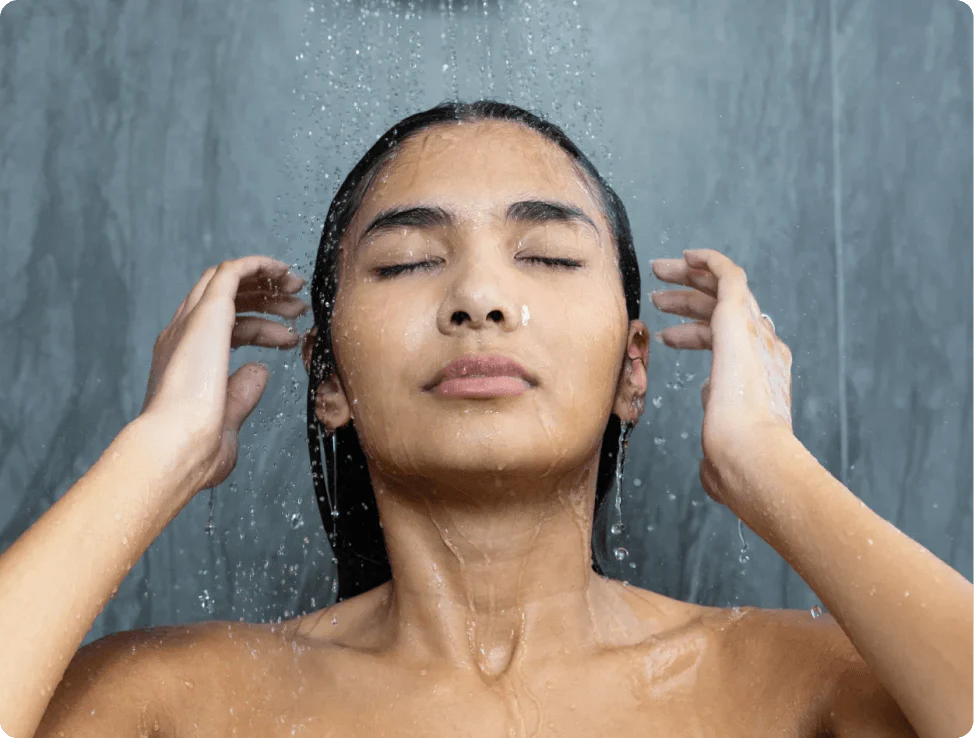 Woman with closed eyes enjoying a shower, water cascading over her hair and shoulders.