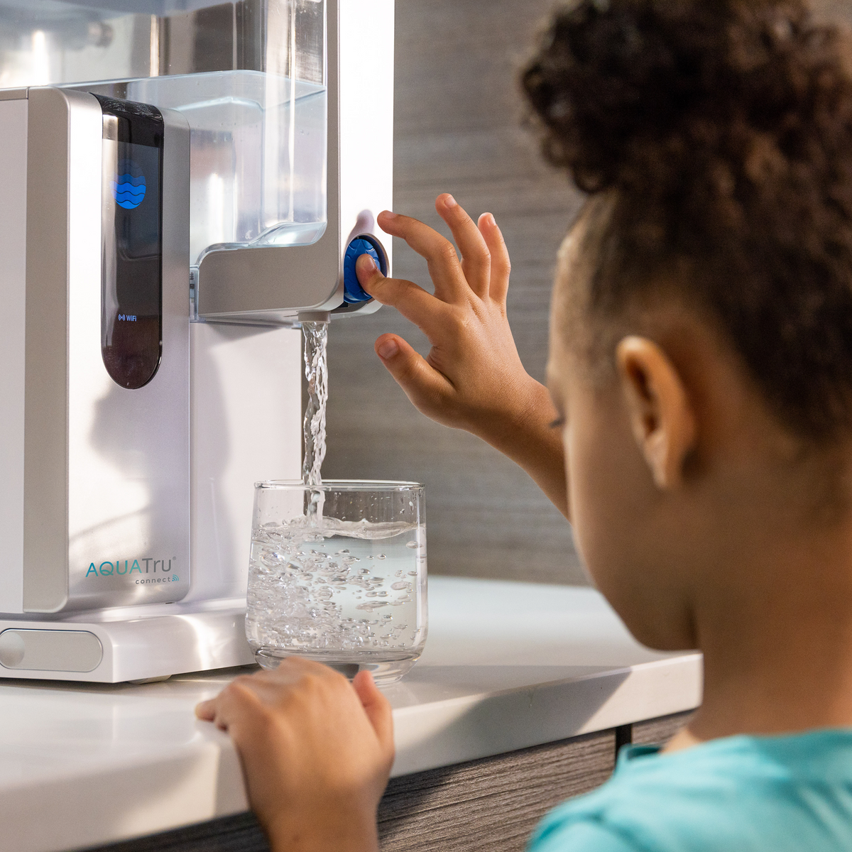AquaTru Classic water purifier with a child filling a glass, featuring a blue button and sleek design.