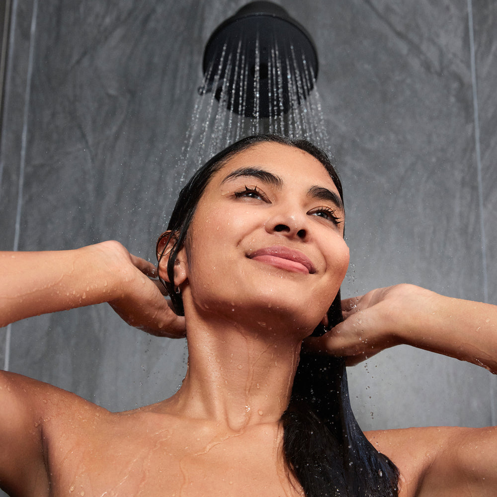 Close-up of a woman smiling while rinsing her hair under a clean stream of water from a shower head.