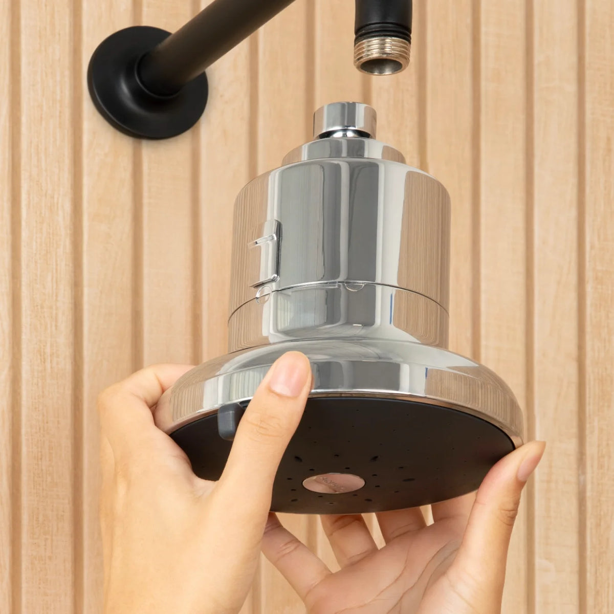 Shiny chrome showerhead being installed, held by hands against a wooden wall.