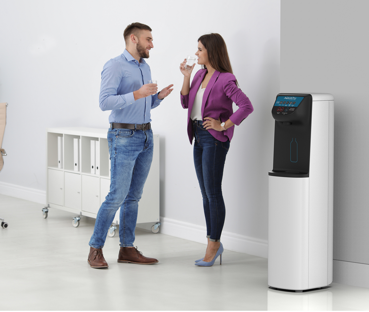 Man and woman chatting by a water cooler in a modern break room, both holding cups.