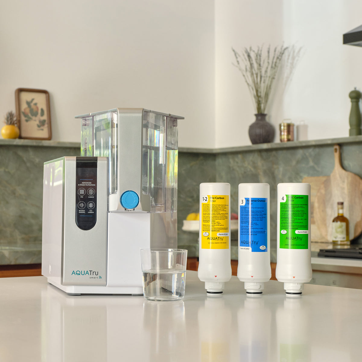 AQUATru water filtration system with three replacement filters and a glass of water on a kitchen countertop.