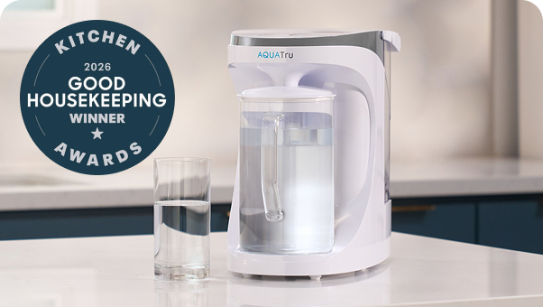 AQUAtru water filtration system next to a glass of water, with a Good Housekeeping Awards badge.