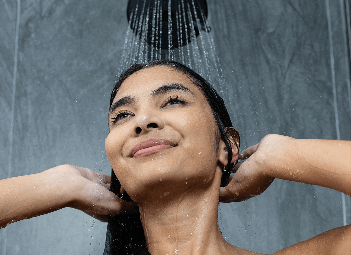 Woman enjoying a shower, water cascading down her hair, with a serene expression on her face.