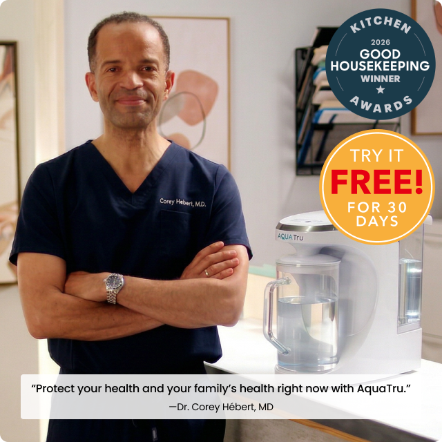 Corey Hébert, M.D. stands beside an AquaTru water purifier, promoting health benefits with a confident smile.