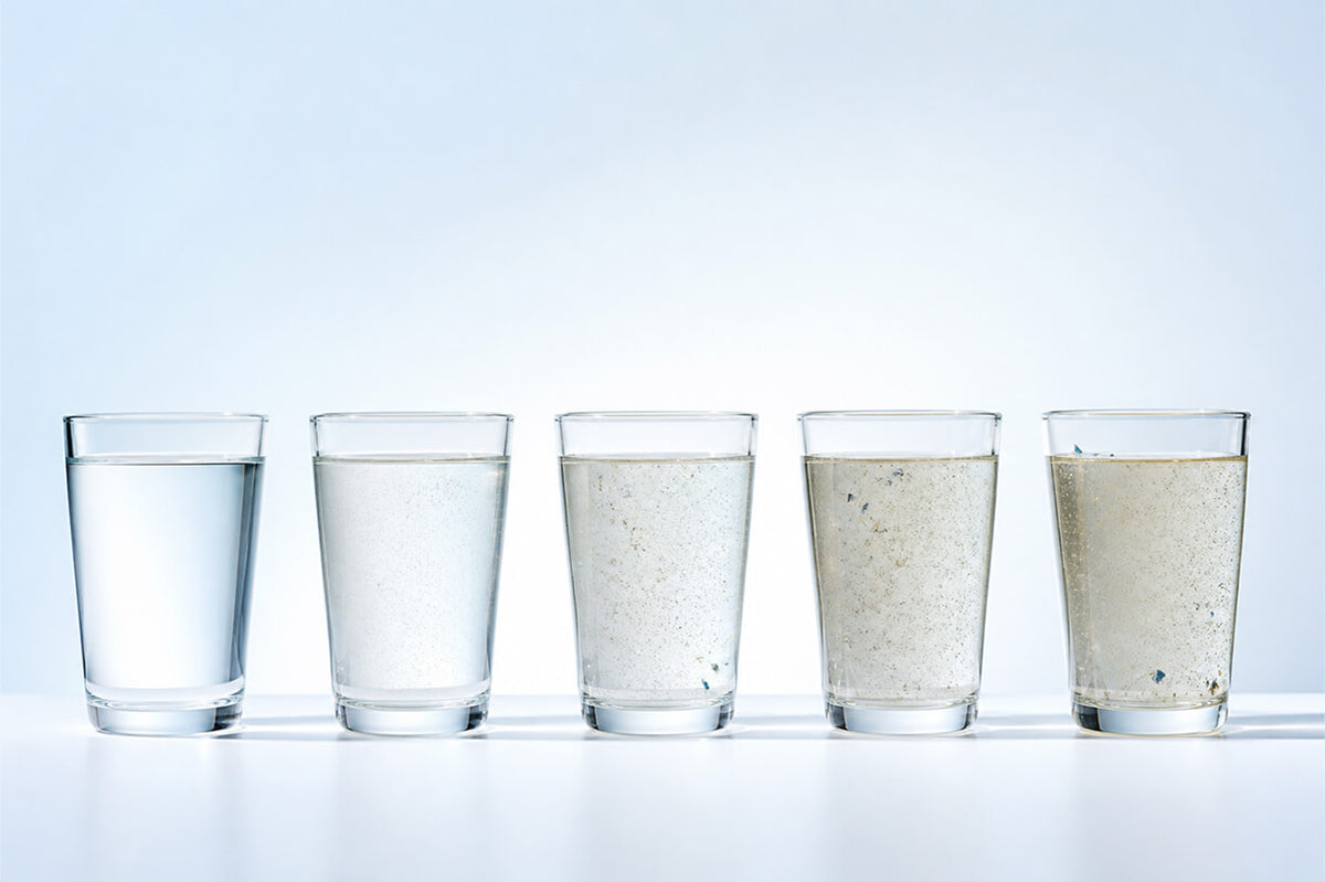 Five glasses of water, each with varying clarity from clear to murky, arranged in a row against a light background.