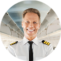 Smiling pilot in uniform with epaulettes, standing inside an airplane cabin.