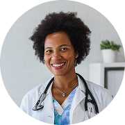 Smiling female doctor with curly hair, wearing a white coat and stethoscope, standing in a bright office setting.