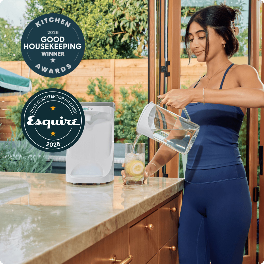 Woman in activewear pouring water from a pitcher into a glass on a kitchen counter, with award badges displayed.