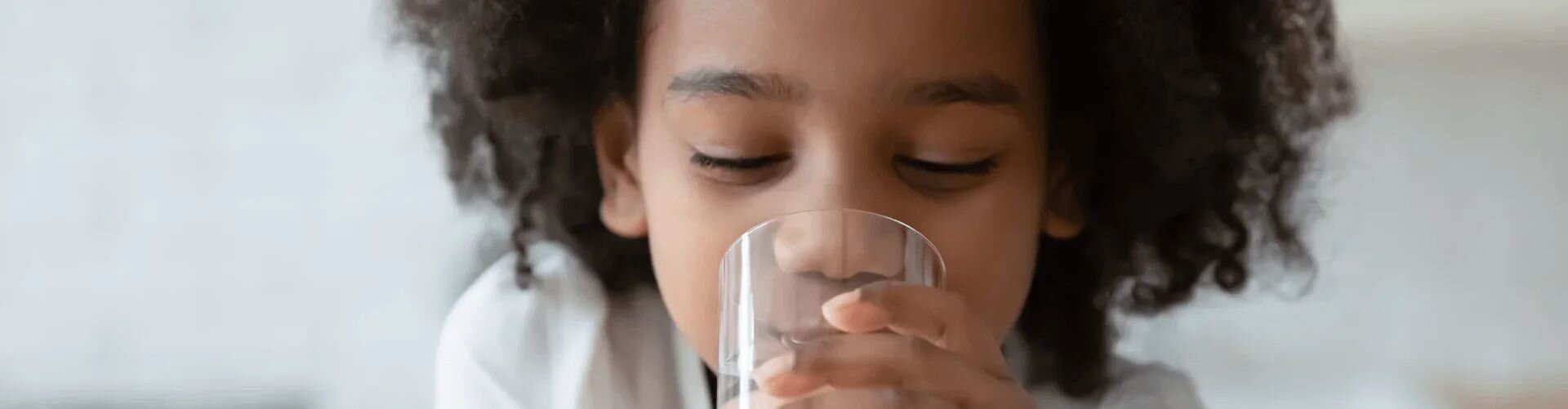 Child drinking from a glass with a plain background