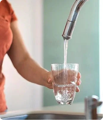 Person filling a glass with water from a faucet.