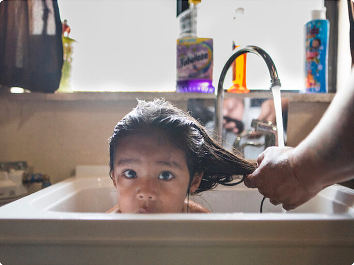 Child in a sink getting their hair washed, with colorful bottles in the background.