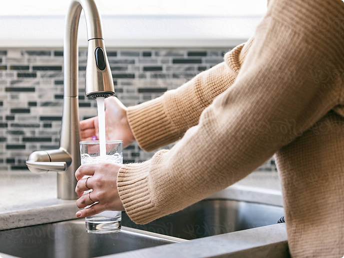 A person fills a glass with water from a modern kitchen faucet over a stylish countertop.