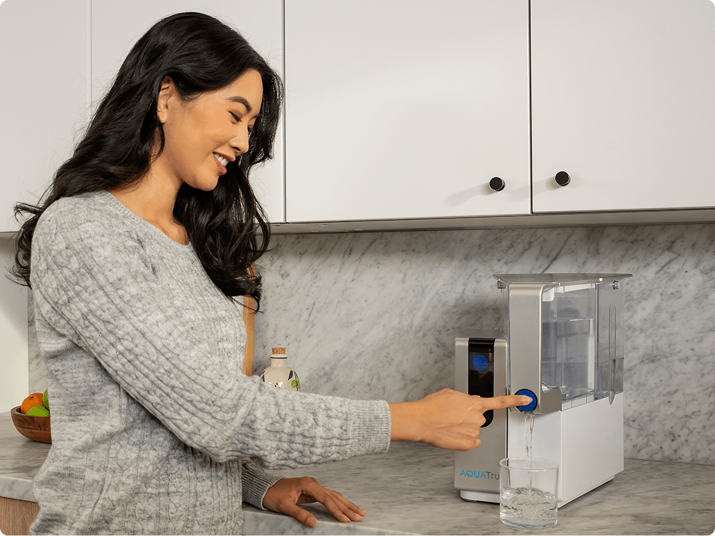 Woman smiling while filling a glass with water from a modern water dispenser on a kitchen counter.