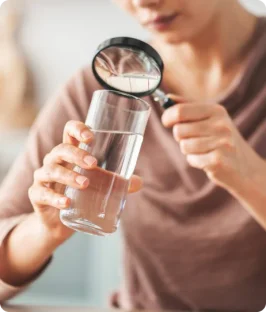 Person holding a glass of water and a magnifying glass, possibly inspecting the water quality.