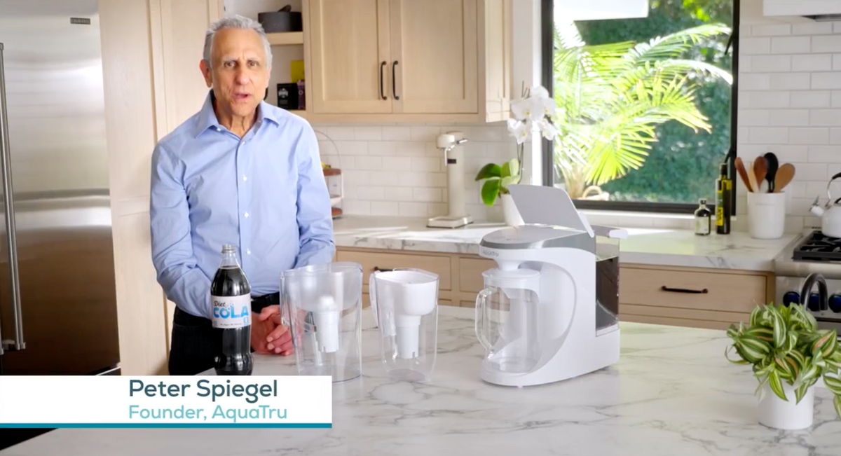 Load video: Demo comparing two pitcher water filters and the AquaTru system after diet cola is poured into each — the pitcher filters fail to clarify the cola, while AquaTru produces crystal-clear water.