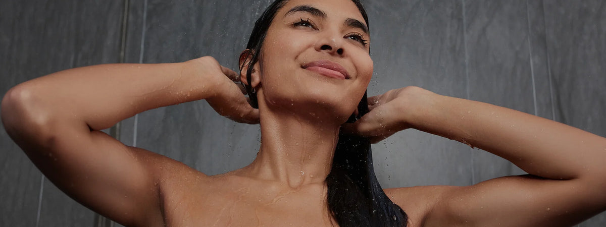 Woman enjoying a refreshing shower, water cascading down her hair and skin, with a serene expression.