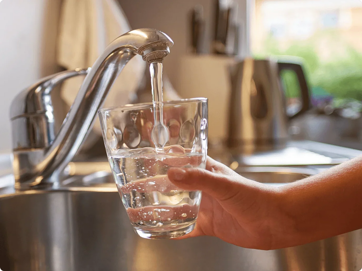 A hand holds a glass under a faucet, filling it with clear water in a kitchen setting.