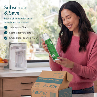 Woman smiling while holding a water filter cartridge, with a delivery box and water purifier in the background.